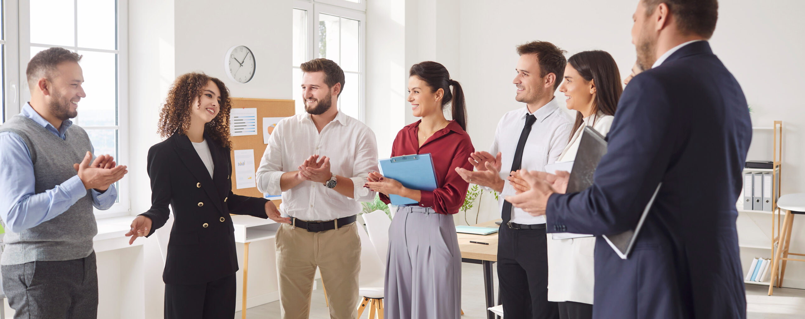 Young woman talking about work project and company finance growth for group of company employees standing in meeting room. Business people applauding female speaker on a conference in office