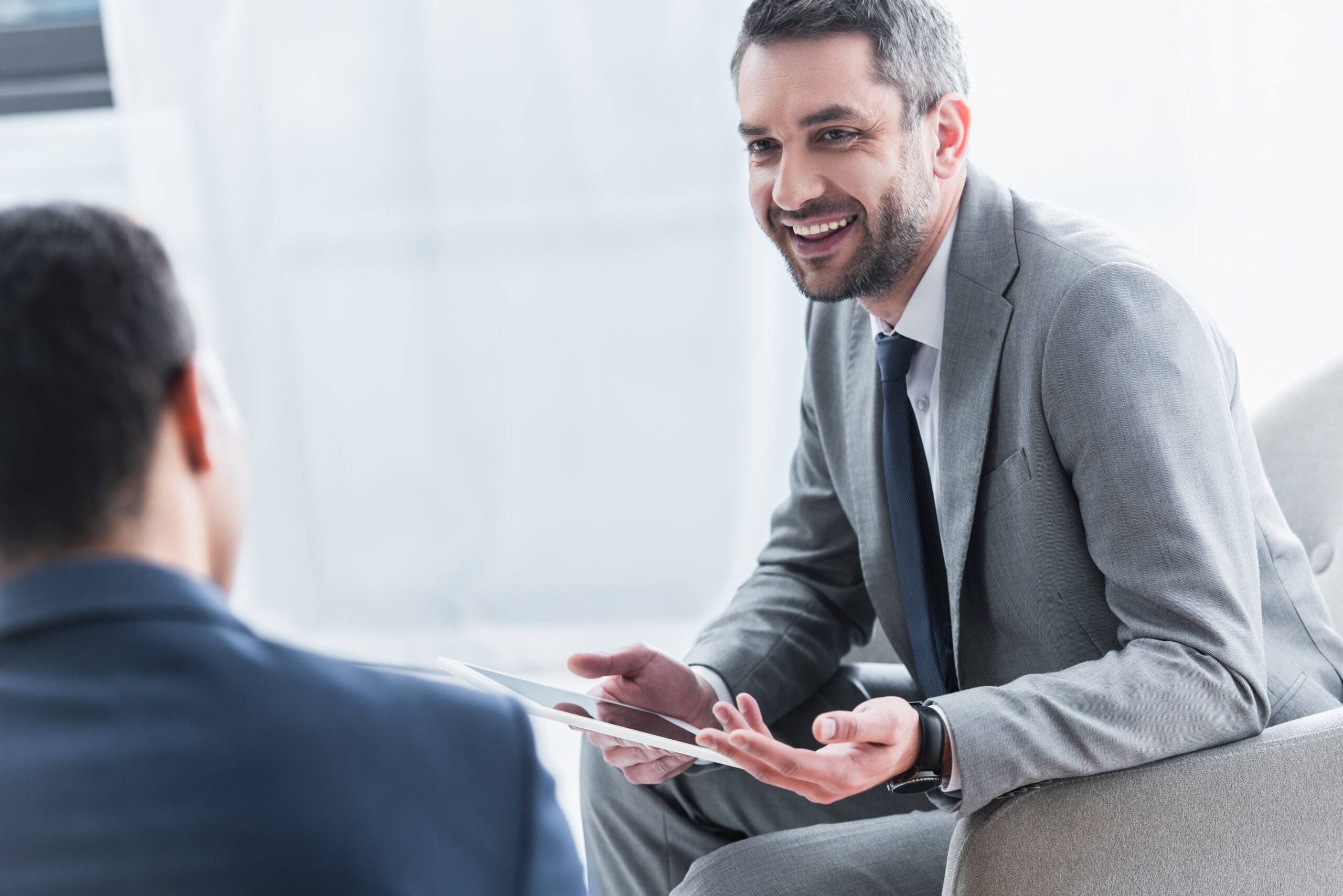 smiling young businessman holding digital tablet and looking at male colleague on foreground